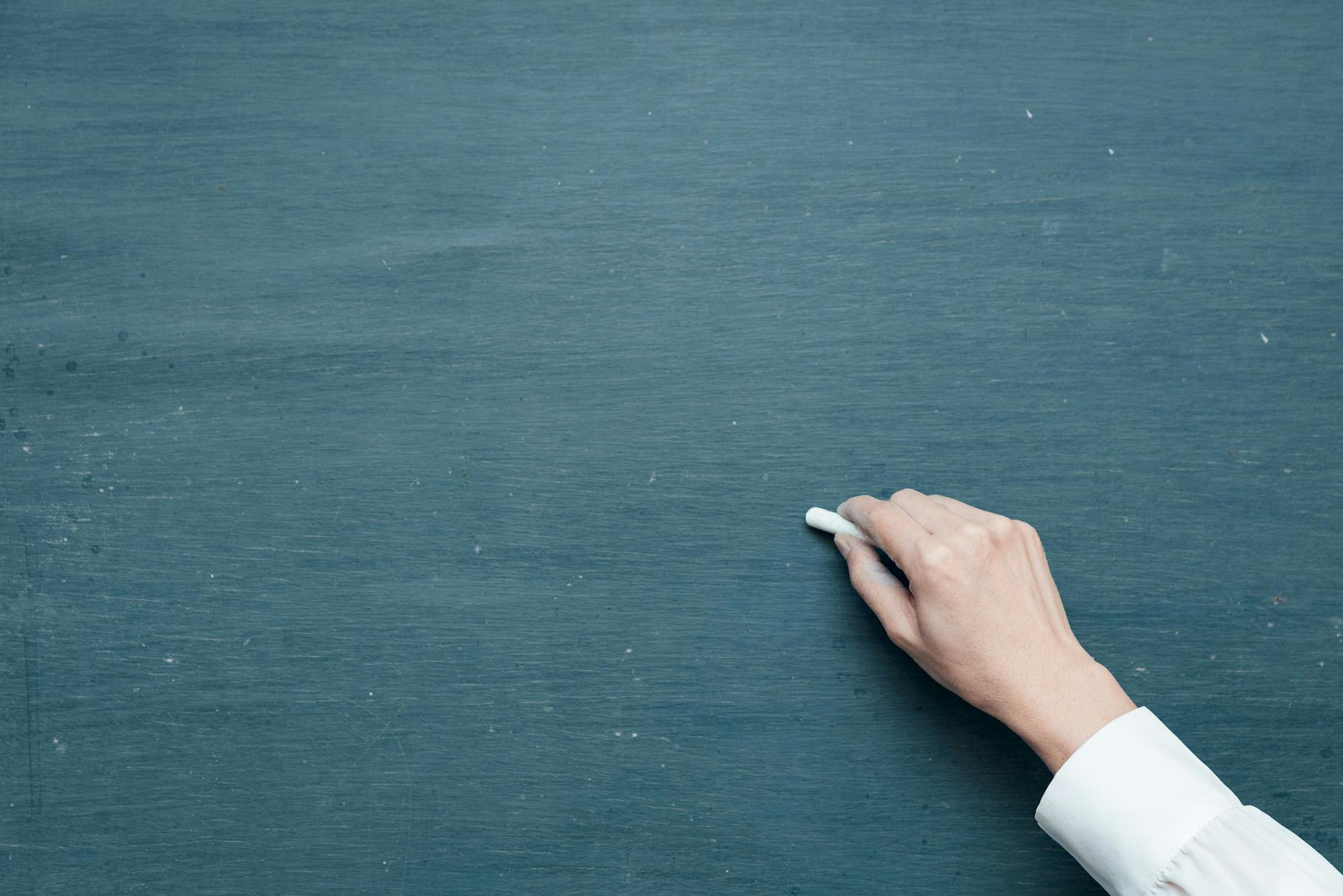 person holding white chalk on green chalkboard
